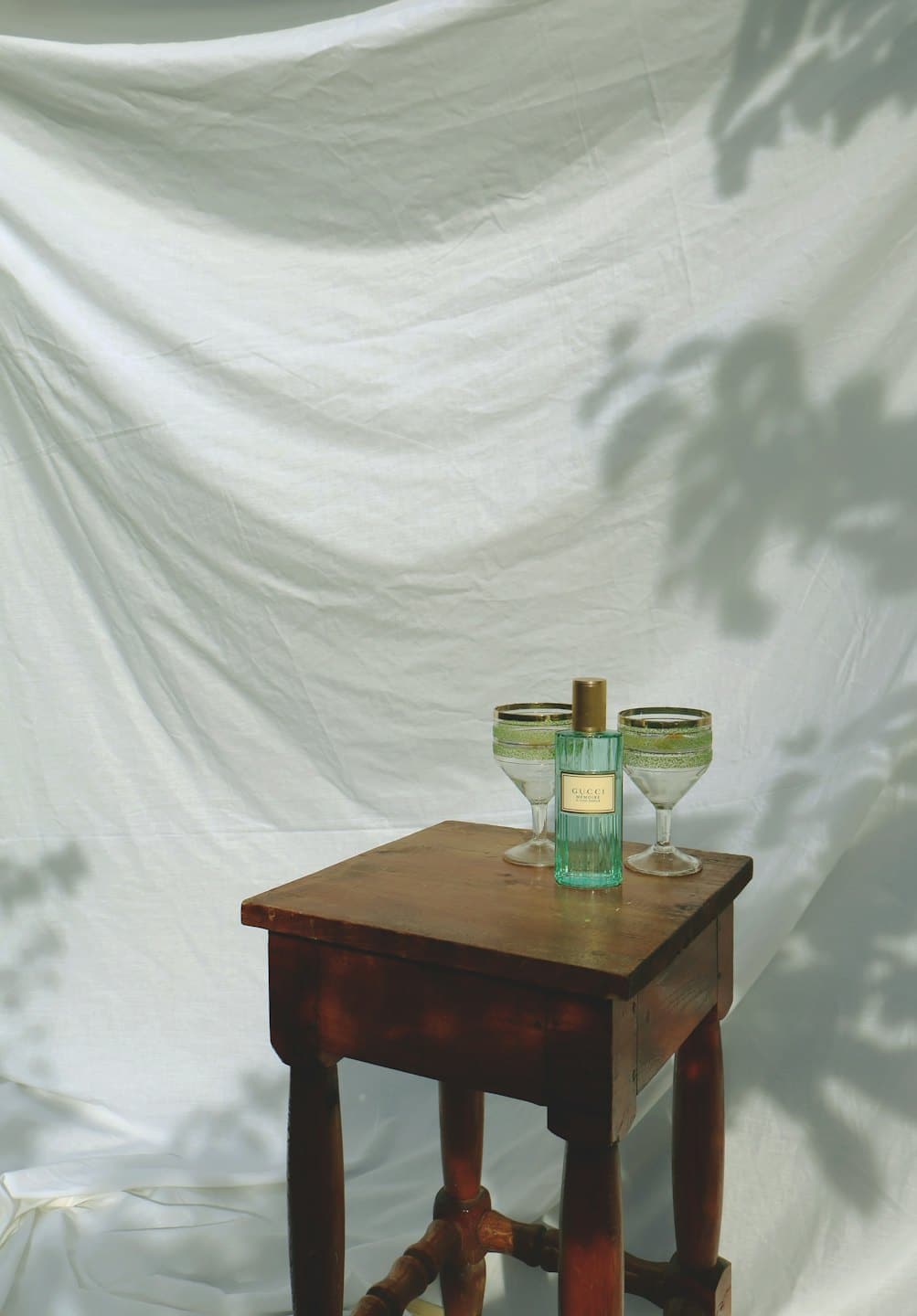 Bouteille de parfum bleu clair entre deux verres à monture dorée sur une table en bois.